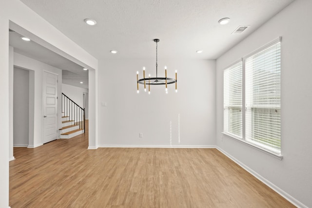 unfurnished room featuring light hardwood / wood-style flooring, a healthy amount of sunlight, a textured ceiling, and an inviting chandelier