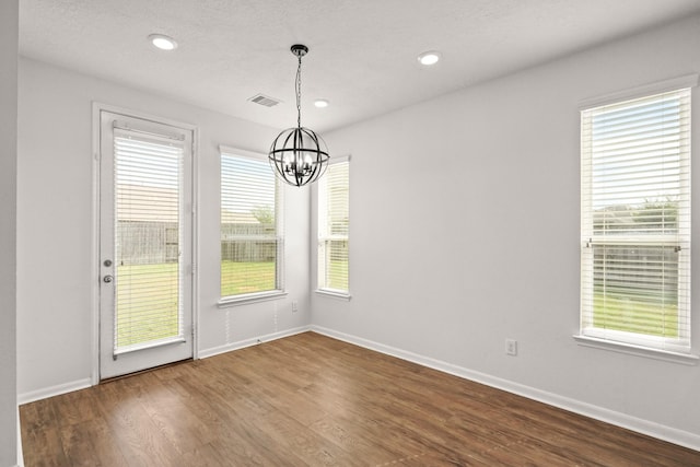 unfurnished dining area featuring wood-type flooring, a textured ceiling, and a notable chandelier