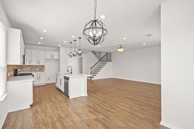 kitchen with white cabinetry, sink, light hardwood / wood-style floors, decorative light fixtures, and a center island with sink