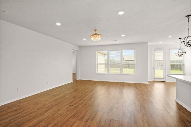 unfurnished living room with a chandelier, wood-type flooring, and a textured ceiling