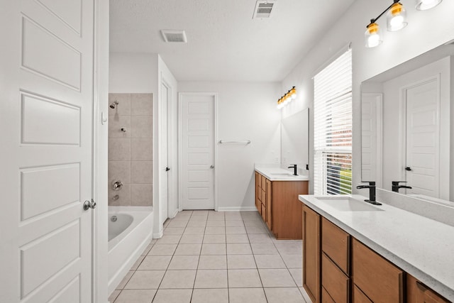 bathroom with tile patterned flooring, vanity, a textured ceiling, and tiled shower / bath