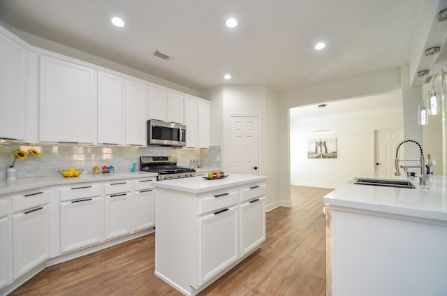 kitchen with white cabinetry, sink, light hardwood / wood-style floors, a kitchen island, and appliances with stainless steel finishes