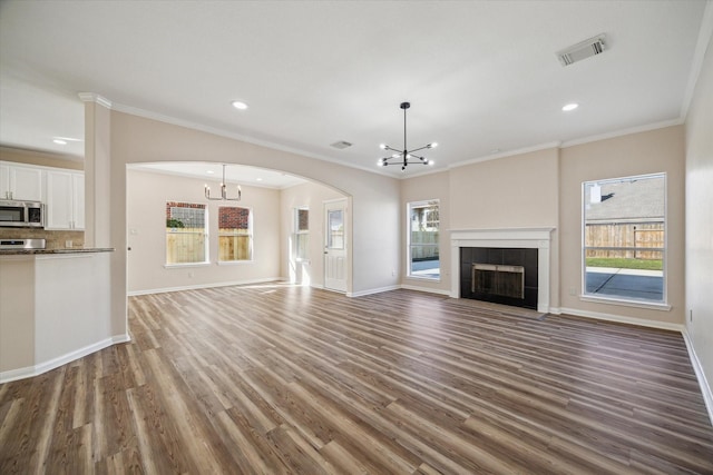 unfurnished living room featuring a notable chandelier, ornamental molding, dark wood-type flooring, and a wealth of natural light