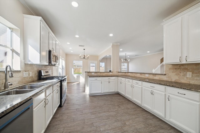 kitchen with kitchen peninsula, appliances with stainless steel finishes, sink, pendant lighting, and light hardwood / wood-style flooring