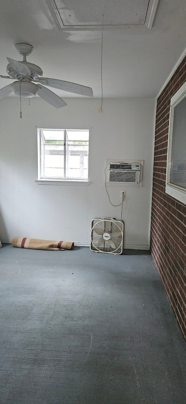 empty room with carpet flooring, attic access, brick wall, a wall mounted AC, and a ceiling fan