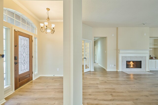 foyer entrance with a tiled fireplace, ornamental molding, light hardwood / wood-style flooring, and a chandelier