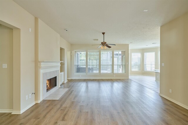 unfurnished living room featuring a tiled fireplace, ceiling fan, and light hardwood / wood-style flooring