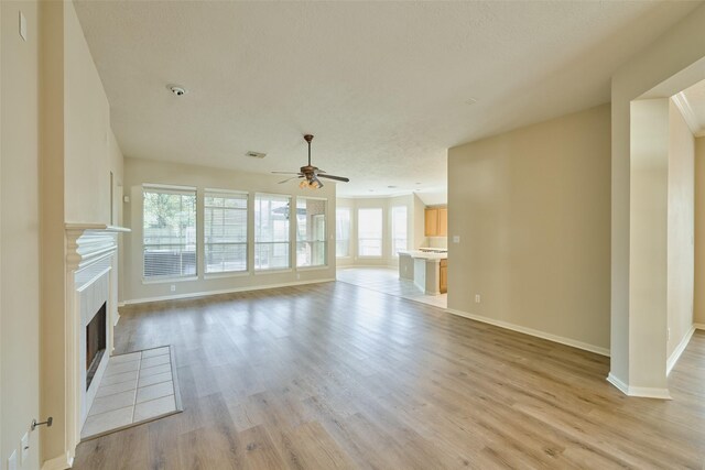 unfurnished living room with a tiled fireplace, ceiling fan, and light hardwood / wood-style floors