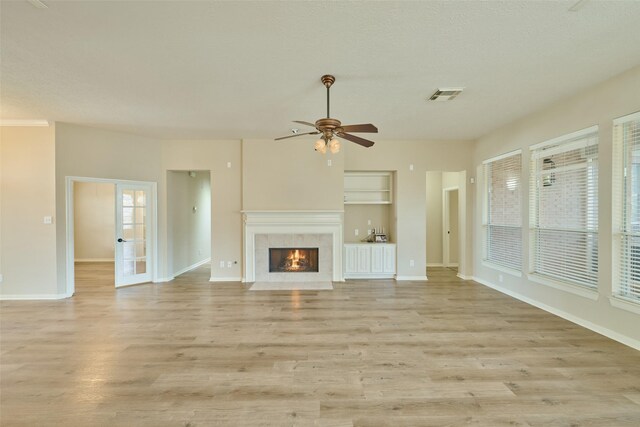 unfurnished living room featuring light wood-type flooring, a tiled fireplace, ceiling fan, and french doors