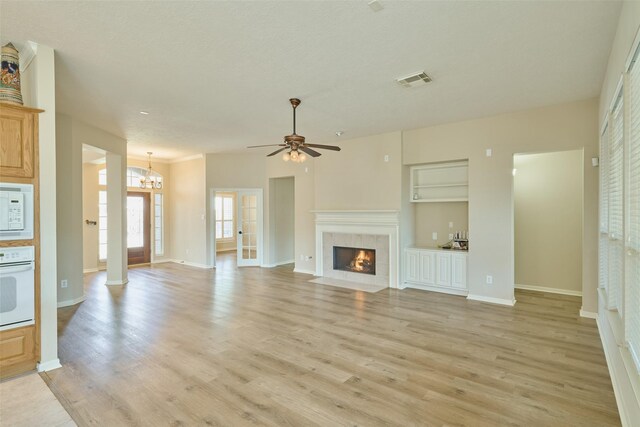 unfurnished living room featuring ceiling fan with notable chandelier, a tile fireplace, light wood-type flooring, and built in features