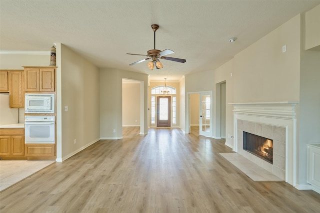 unfurnished living room with a tile fireplace, a textured ceiling, ceiling fan, and light hardwood / wood-style floors