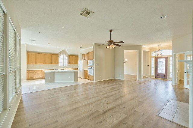 unfurnished living room featuring light hardwood / wood-style flooring, lofted ceiling, and ceiling fan with notable chandelier