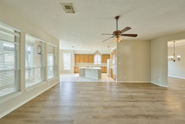 unfurnished living room with ceiling fan with notable chandelier, a textured ceiling, light hardwood / wood-style floors, and lofted ceiling