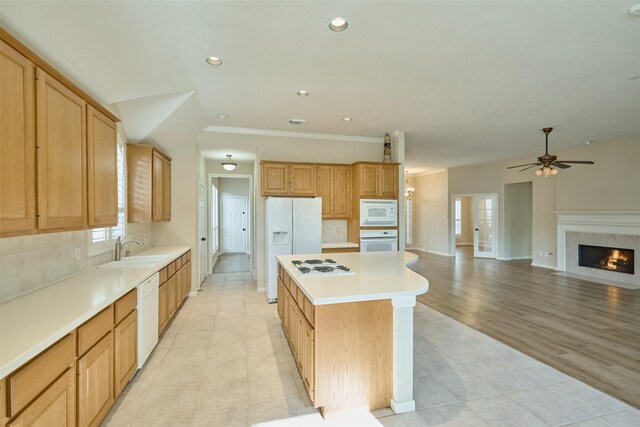 kitchen with white appliances, a kitchen island, backsplash, a tiled fireplace, and sink