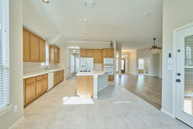 kitchen featuring white appliances, light tile patterned floors, decorative backsplash, a kitchen island, and ceiling fan with notable chandelier