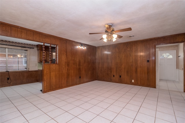 tiled empty room featuring ceiling fan, a textured ceiling, and wooden walls