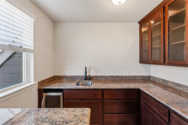 kitchen featuring wine cooler, stone counters, and sink