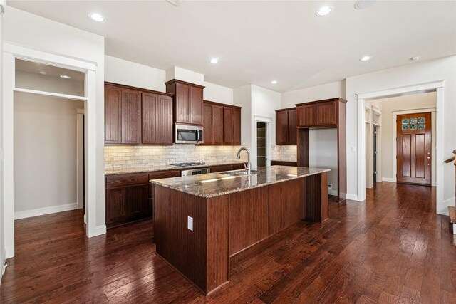 kitchen featuring appliances with stainless steel finishes, dark wood-type flooring, sink, a center island with sink, and dark stone countertops