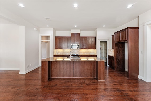 kitchen featuring dark hardwood / wood-style floors, light stone countertops, stainless steel appliances, and a kitchen island with sink