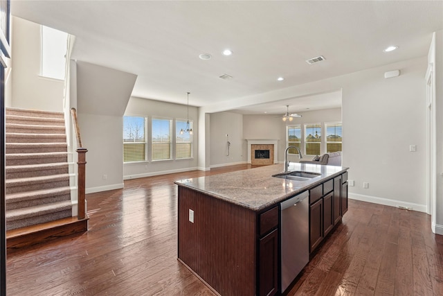 kitchen featuring a center island with sink, sink, stainless steel dishwasher, dark hardwood / wood-style floors, and a tiled fireplace