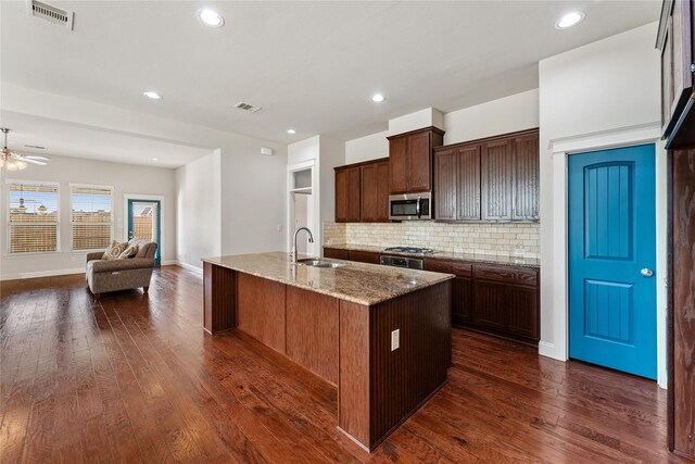 kitchen featuring sink, dark wood-type flooring, light stone counters, a center island with sink, and appliances with stainless steel finishes