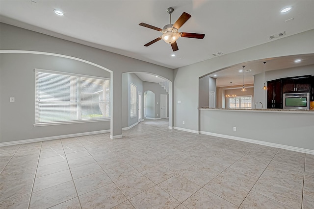 unfurnished living room with plenty of natural light, sink, light tile patterned floors, and ceiling fan with notable chandelier