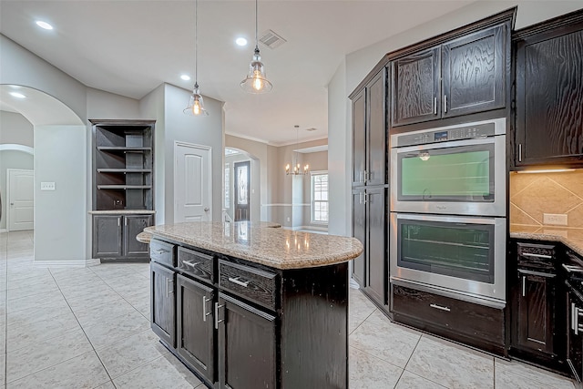 kitchen with a center island, hanging light fixtures, stainless steel double oven, an inviting chandelier, and light stone counters