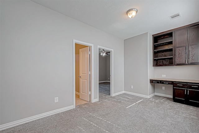 unfurnished office featuring light carpet, built in desk, and ceiling fan