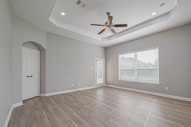 empty room with a tray ceiling, ceiling fan, and light hardwood / wood-style floors