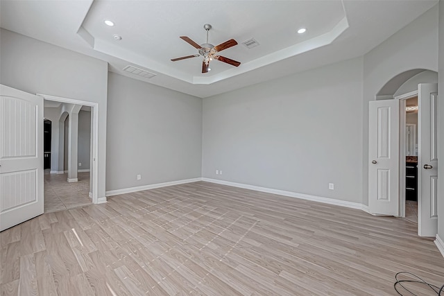 spare room with a tray ceiling, ceiling fan, and light hardwood / wood-style floors