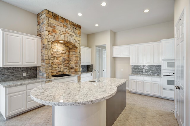 kitchen with decorative backsplash, white cabinetry, a center island with sink, and white appliances