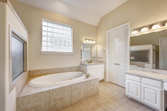 bathroom featuring tile patterned floors, vanity, a relaxing tiled tub, and vaulted ceiling