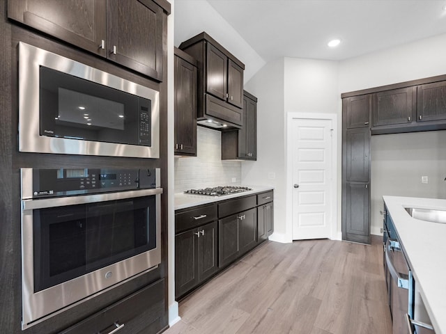 kitchen with sink, appliances with stainless steel finishes, tasteful backsplash, dark brown cabinets, and light hardwood / wood-style floors