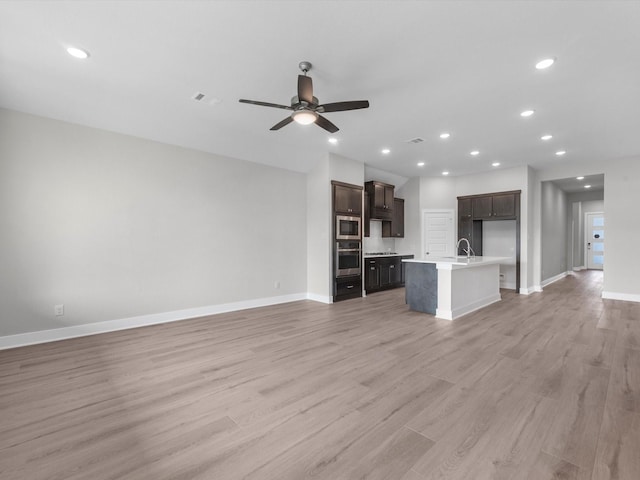 unfurnished living room featuring ceiling fan, light wood-type flooring, and sink