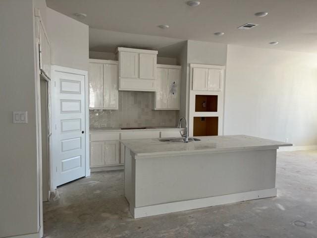 kitchen featuring tasteful backsplash, white cabinetry, a center island with sink, and sink