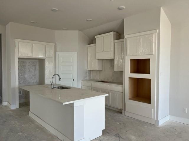 kitchen with sink, built in features, an island with sink, cooktop, and white cabinetry