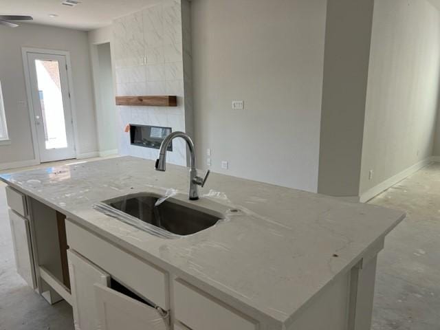 kitchen featuring a tile fireplace, white cabinetry, sink, light stone countertops, and an island with sink