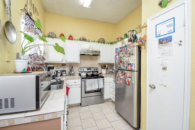 kitchen with decorative backsplash, tile counters, light tile patterned flooring, white cabinetry, and stainless steel appliances