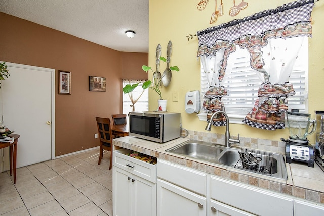 kitchen featuring tile counters, sink, light tile patterned floors, a textured ceiling, and white cabinets