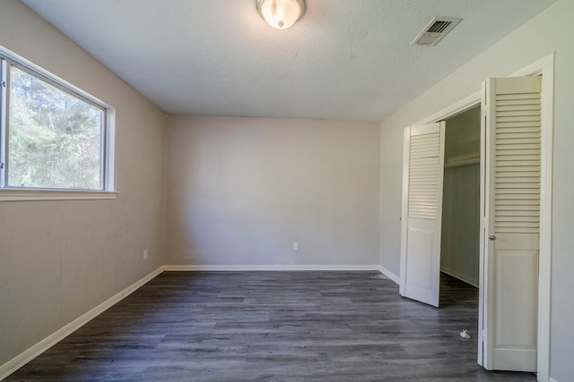 unfurnished bedroom with a textured ceiling, a closet, and dark wood-type flooring