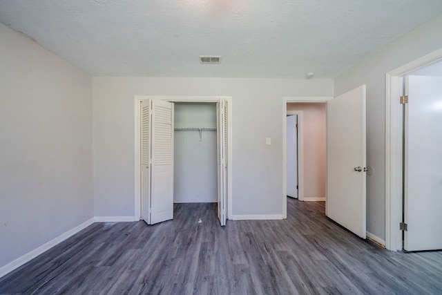 unfurnished bedroom featuring a textured ceiling, dark hardwood / wood-style floors, and a closet