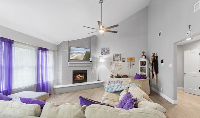 living room featuring ceiling fan, light wood-type flooring, a fireplace, and high vaulted ceiling