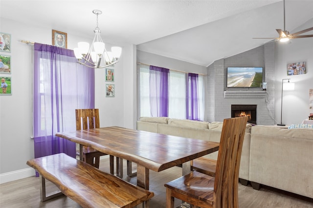 dining area with a fireplace, ceiling fan with notable chandelier, lofted ceiling, and light hardwood / wood-style flooring