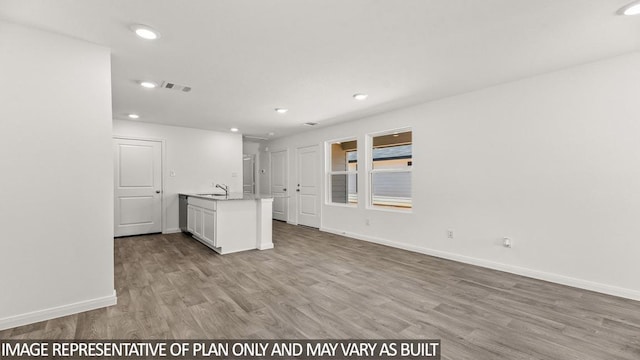 interior space featuring light hardwood / wood-style flooring, white cabinets, an island with sink, and sink