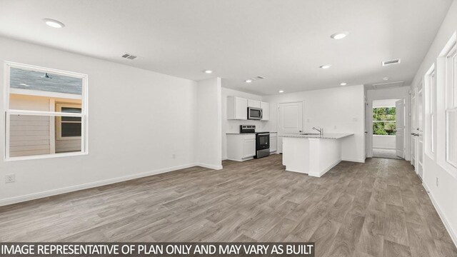 kitchen with white cabinets, light hardwood / wood-style floors, a center island with sink, and appliances with stainless steel finishes