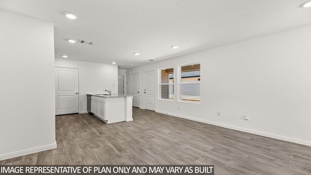 interior space with light hardwood / wood-style floors, sink, white cabinetry, and an island with sink