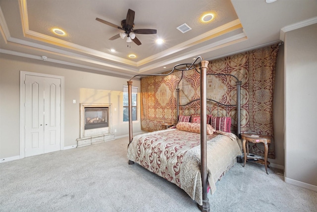 carpeted bedroom featuring a raised ceiling, ceiling fan, a closet, and crown molding