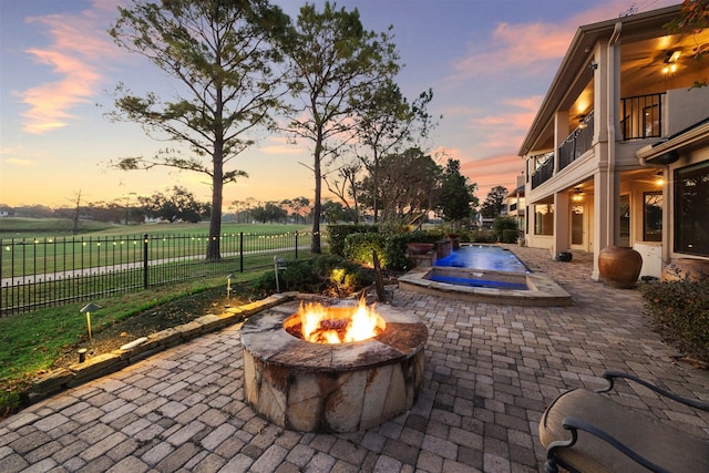 patio terrace at dusk with a pool, a balcony, and a fire pit