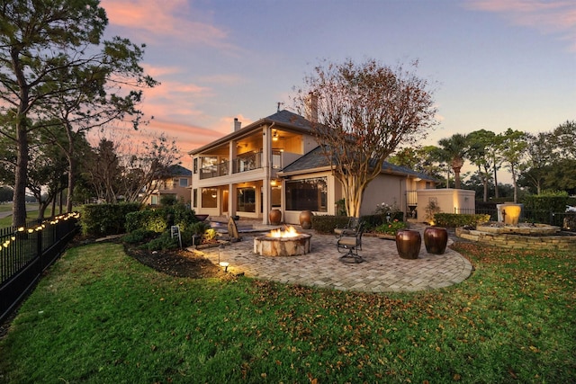 back house at dusk featuring a lawn, a patio area, a balcony, and an outdoor fire pit