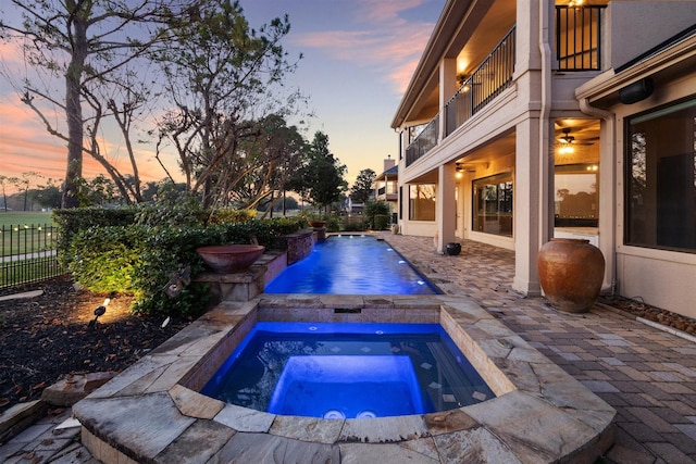 pool at dusk with an in ground hot tub